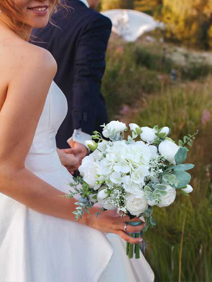 a bride holding a bouquet of white flowers in her hand while standing next to the groom