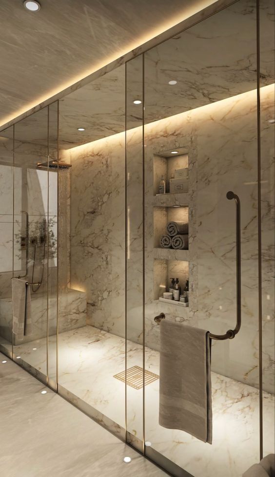 a bathroom with marble walls and flooring is lit by recessed lighting from the ceiling