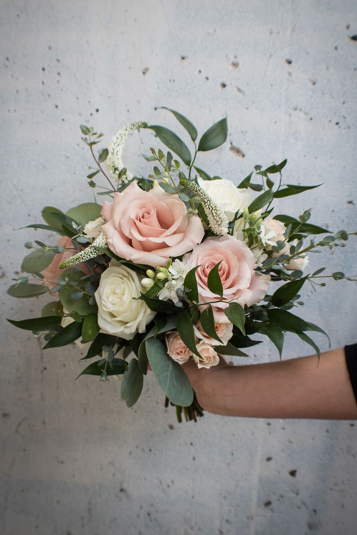 a person holding a bouquet of pink and white flowers with greenery on the side