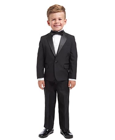 a young boy in a tuxedo and bow tie smiles at the camera while standing against a white background