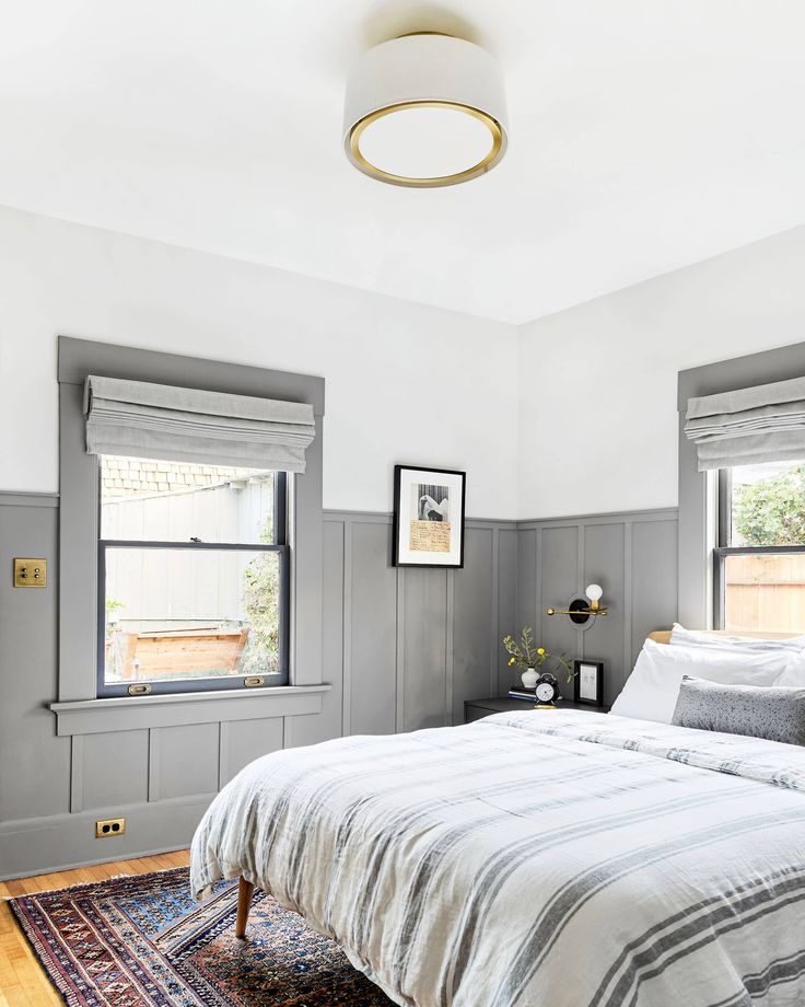 a bed sitting in a bedroom next to two windows and a rug on the floor