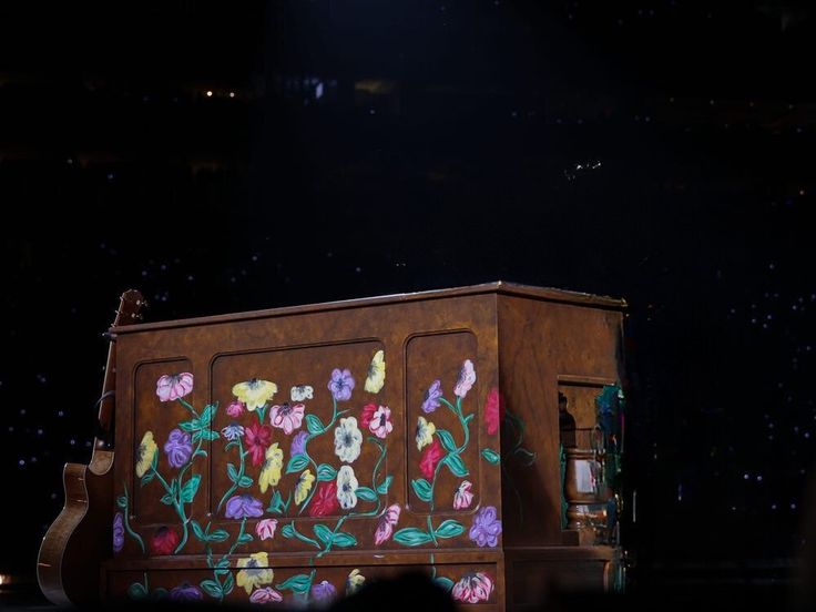 a large wooden box with flowers painted on it's sides and lights in the background