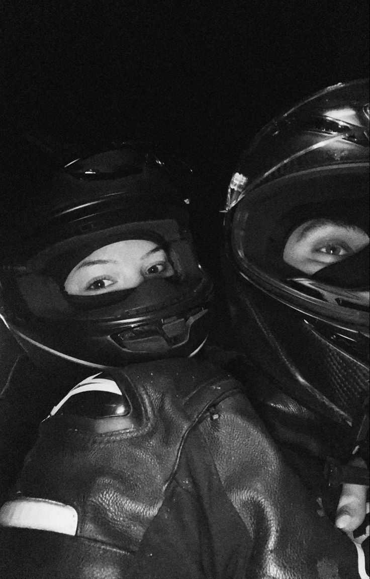 black and white photograph of two people wearing motorcycle helmets, one looking at the camera