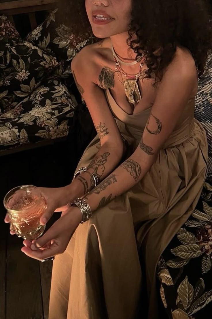 a woman sitting on a couch holding a wine glass in her right hand and tattoos on her left arm