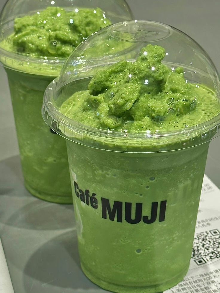 two plastic cups filled with green liquid on top of a table next to each other