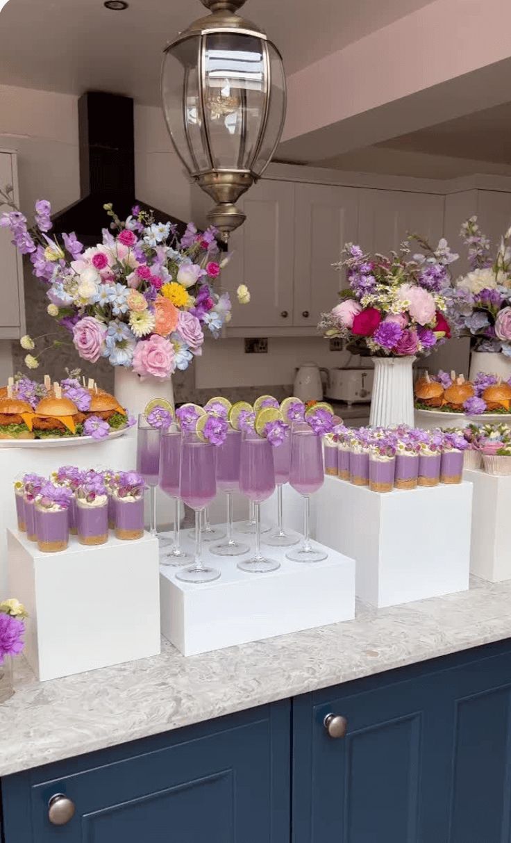 there are many cupcakes on the counter with purple frosting and flowers in vases