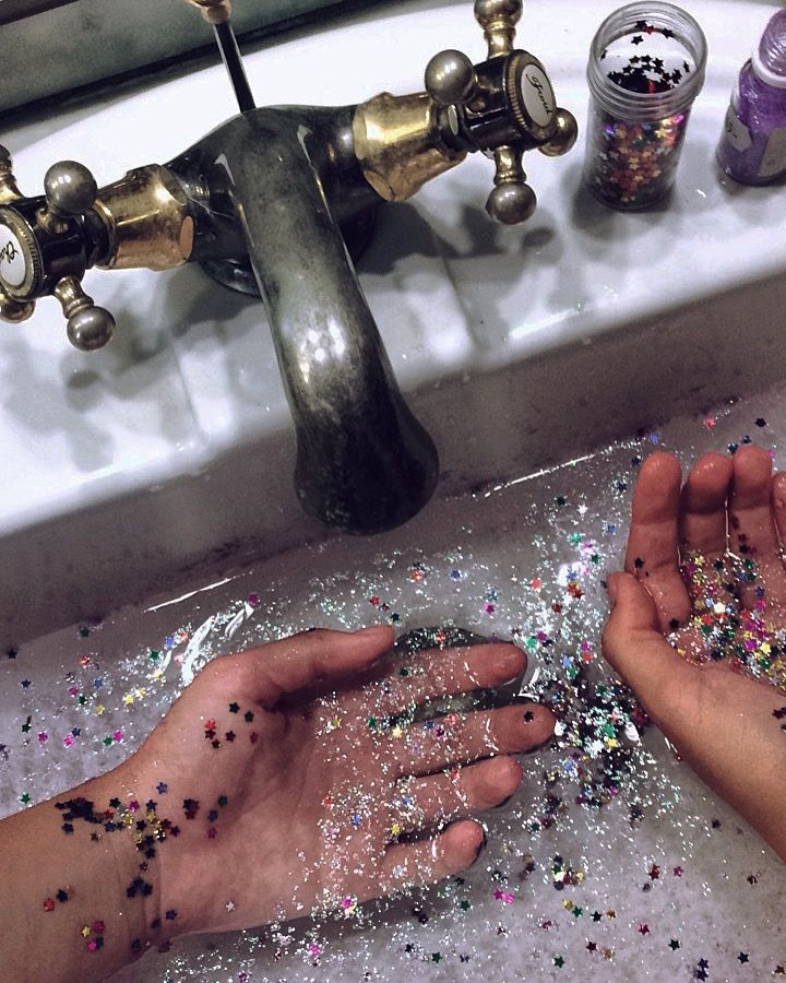 two hands are sprinkled with glitter in front of a sink faucet