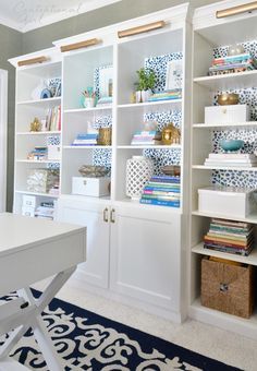 a white bookcase filled with lots of books on top of a blue and white rug