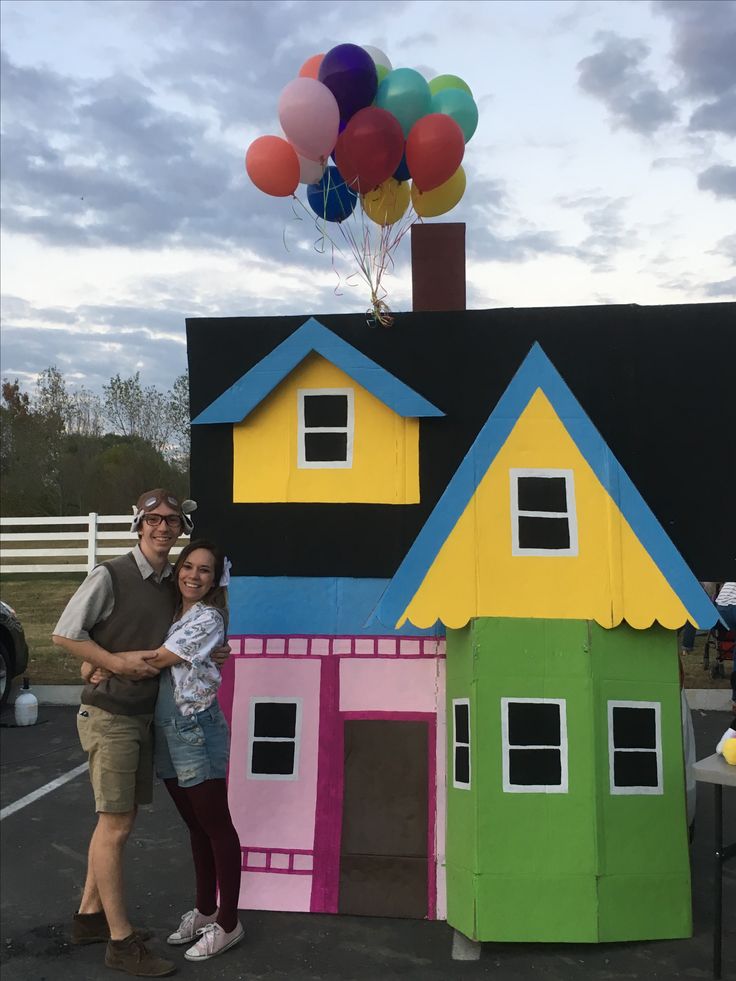 a man and woman standing in front of a house made out of cardboard with balloons