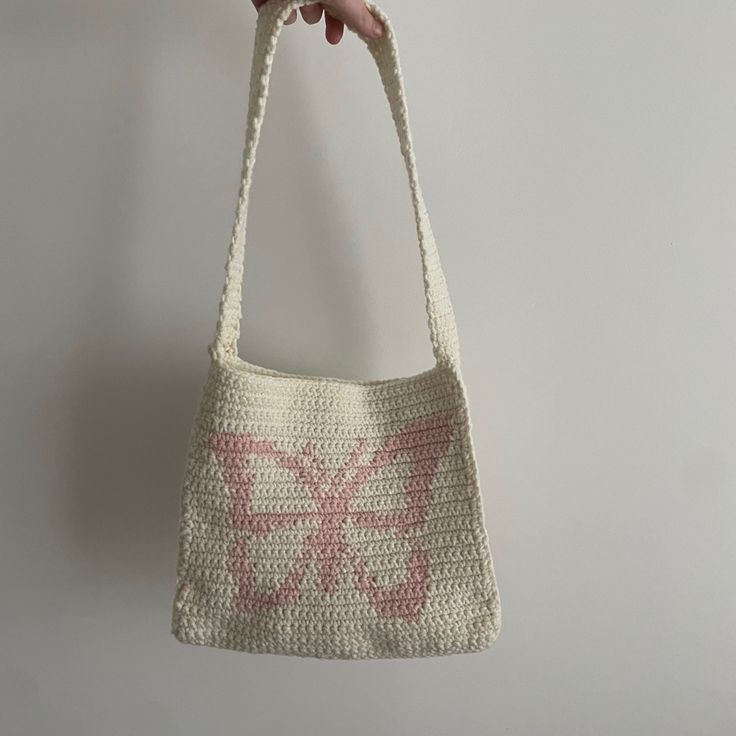 a crocheted bag hanging from a hook on a wall with a flower in it