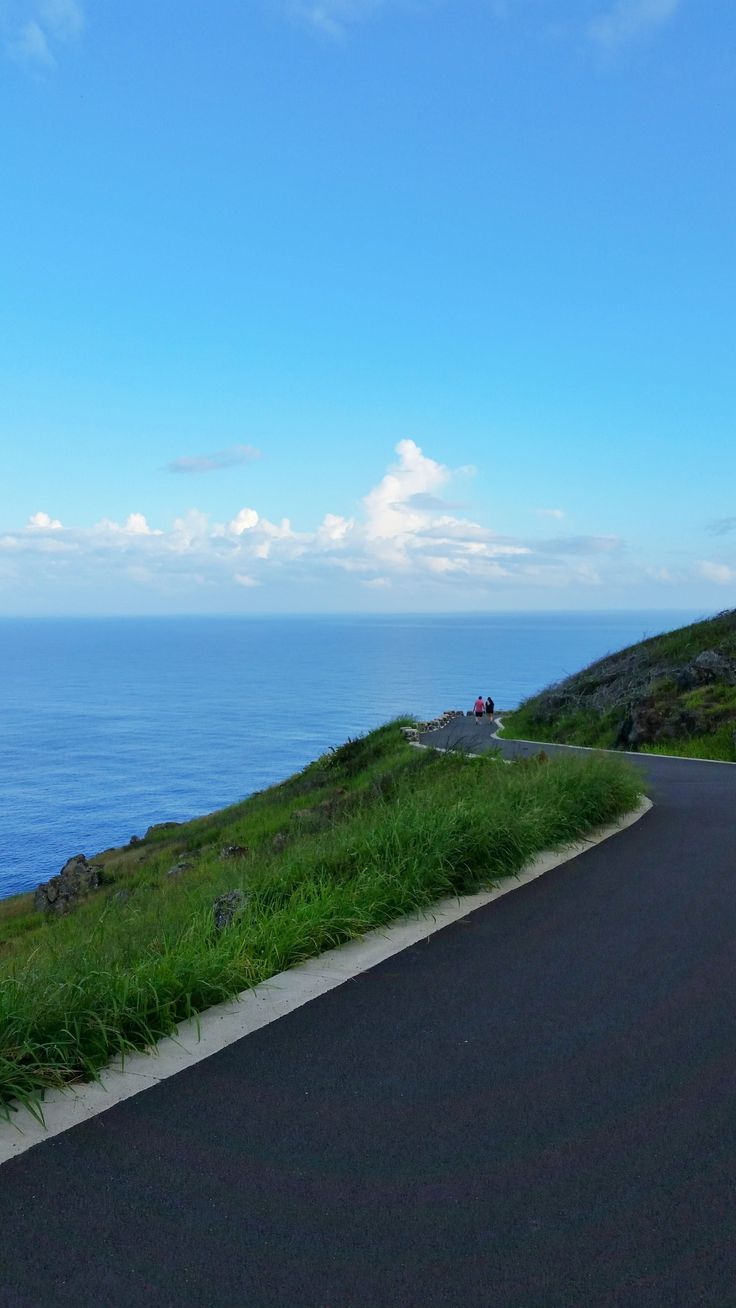 an empty road next to the ocean on a sunny day with blue sky and clouds