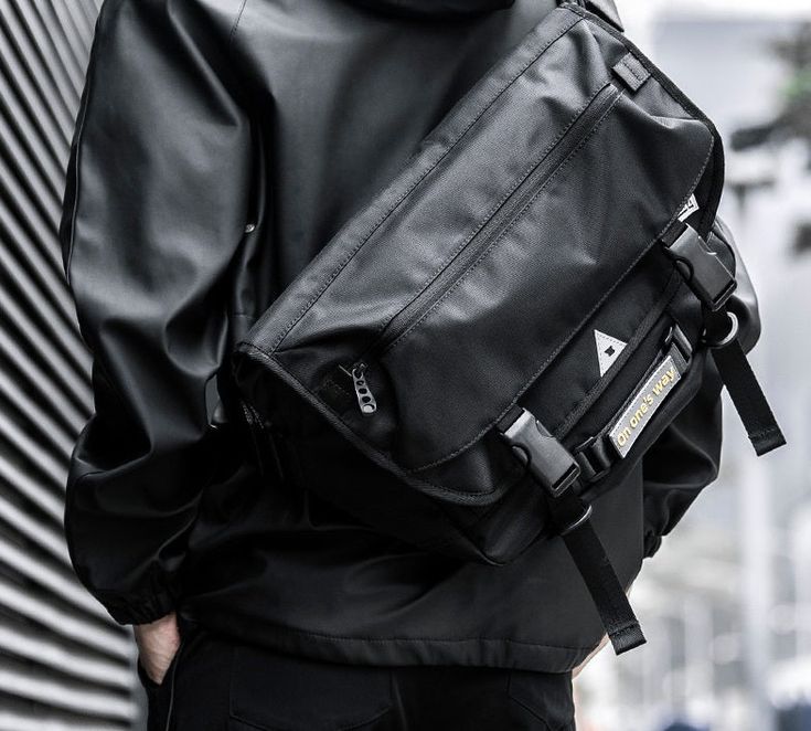 a man wearing a black leather backpack with his back turned to the camera while standing in front of a building