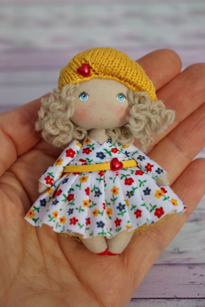 a hand holding a small doll wearing a yellow hat and dress with flowers on it