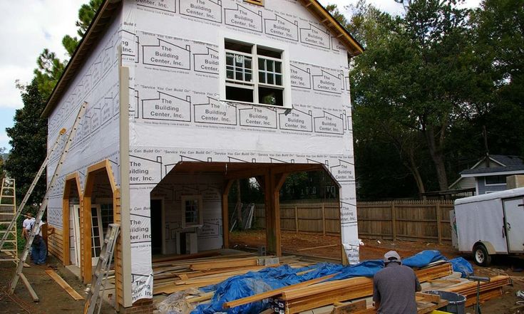 a man standing in front of a white house under construction with wood framing around it