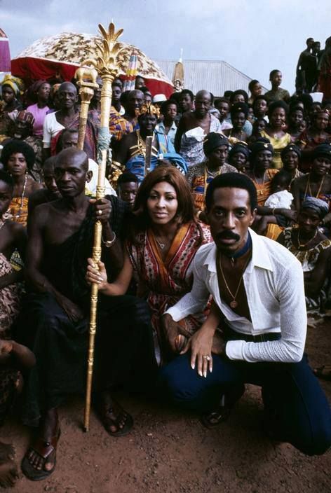 a group of people sitting on the ground with one holding a stick and posing for a photo