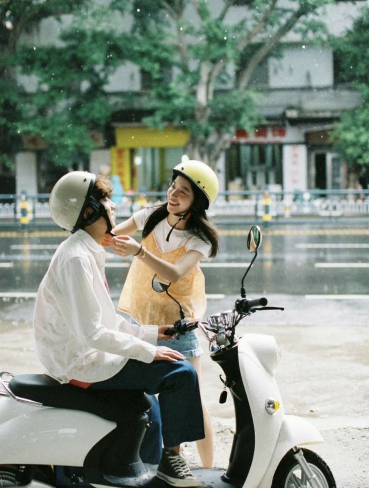 two people sitting on a scooter in the rain and one person is brushing her hair