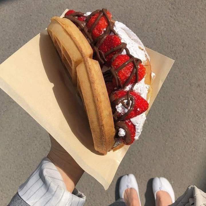 a person holding a pastry with chocolate and strawberries on it