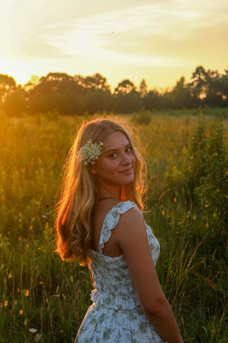 a beautiful young woman standing in a field at sunset