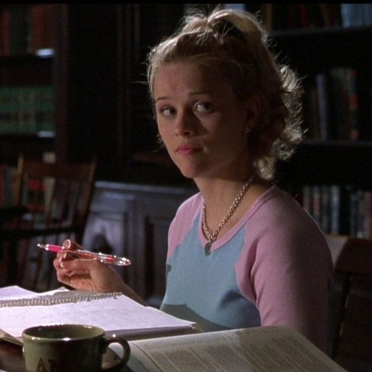 a woman sitting at a table with a book and pen in her hand while looking at the camera