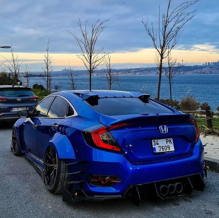 the rear end of a blue car parked on the side of the road next to water