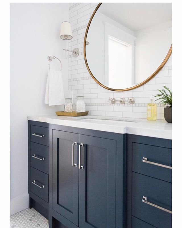 a bathroom with blue cabinets and a round mirror