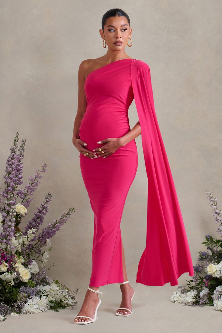 a pregnant woman wearing a pink gown and matching shawl stands in front of flowers