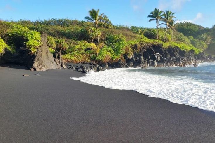 the black sand beach has waves coming in from the ocean and palm trees on the hillside