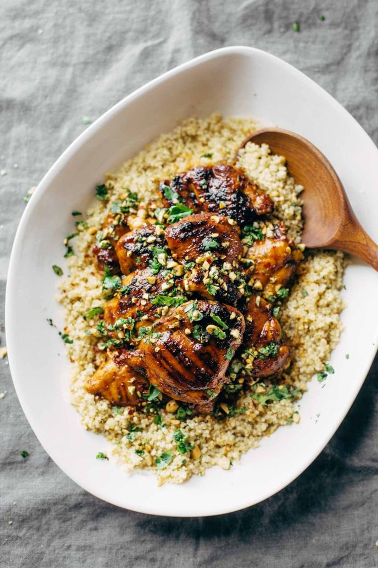 a white bowl filled with rice and chicken on top of a table next to a wooden spoon