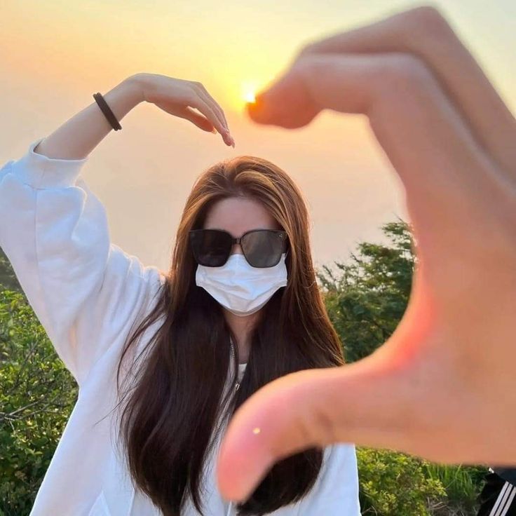 a woman wearing a face mask and pointing at the sun with her hand in front of her