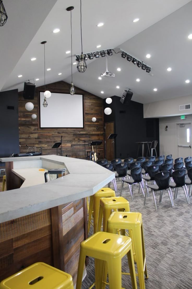 an empty bar with yellow stools in front of it and a projector screen on the wall