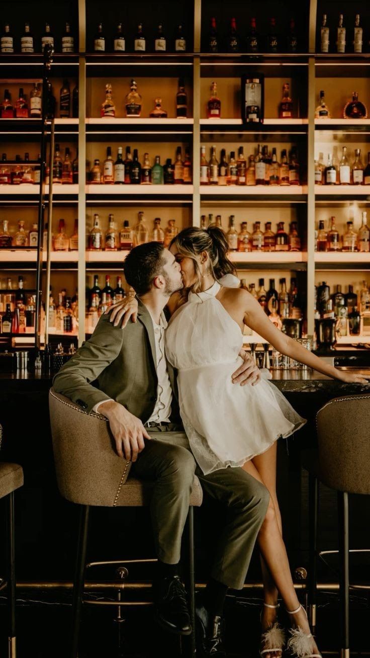 a man and woman kissing in front of shelves with liquor bottles on the wall behind them