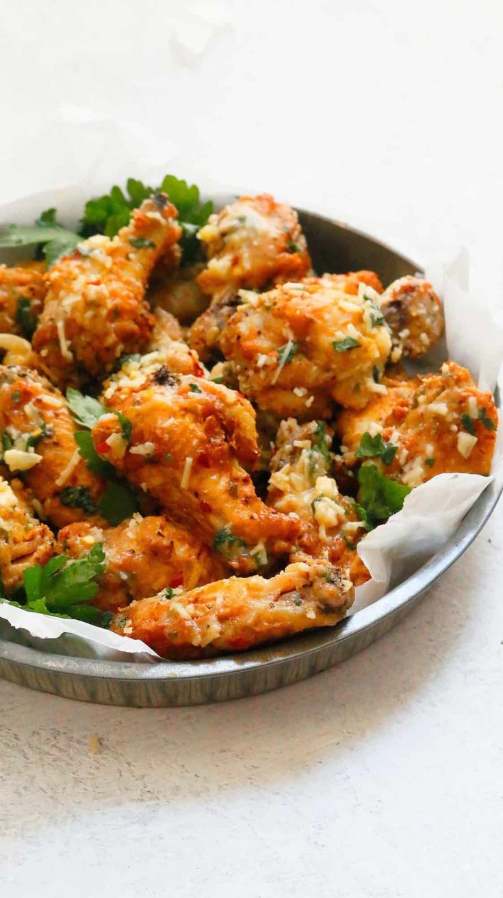 a metal bowl filled with chicken wings covered in parsley