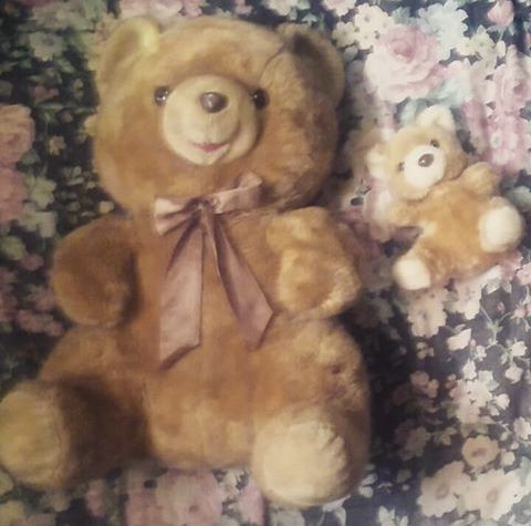 a brown teddy bear laying on top of a bed next to a small stuffed animal