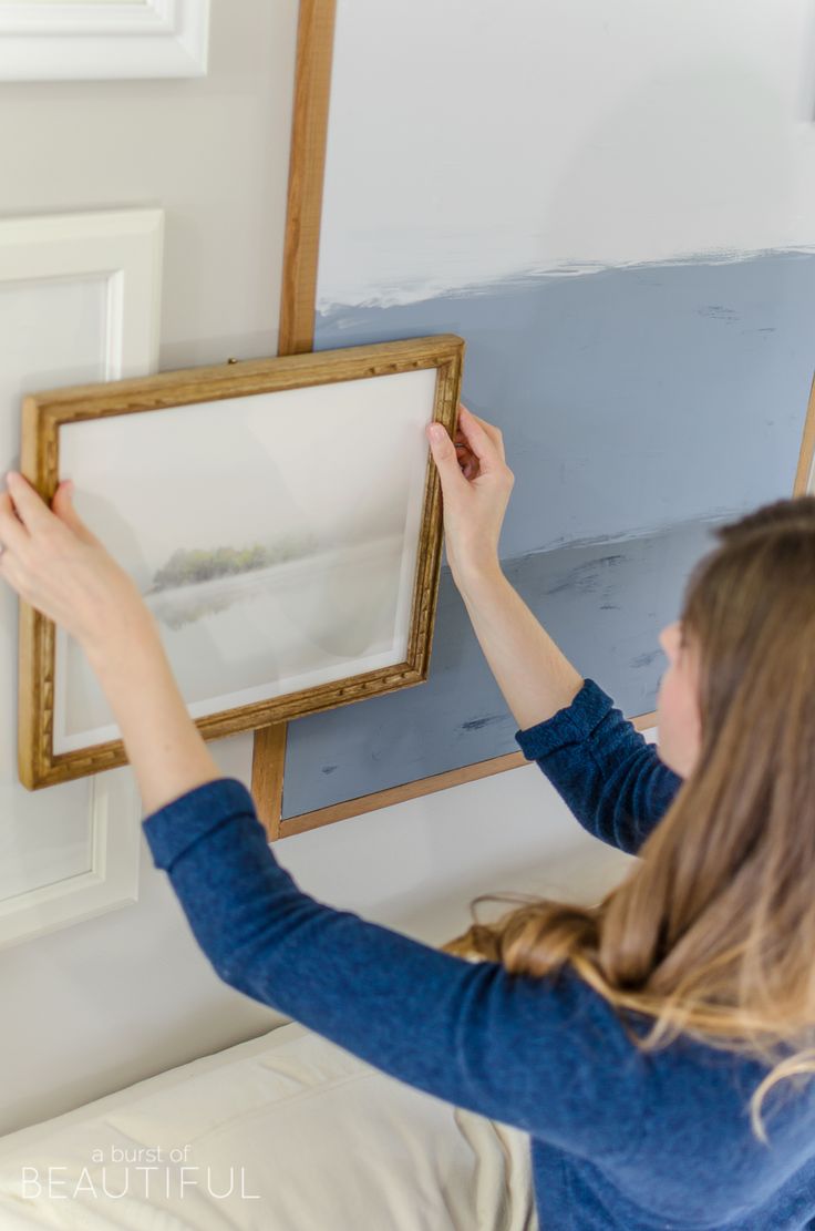 a woman is hanging pictures on the wall