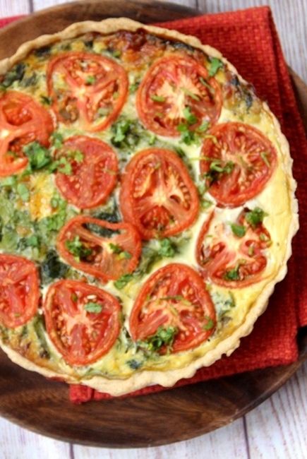 a quiche with tomatoes and cheese on a wooden plate next to a red napkin