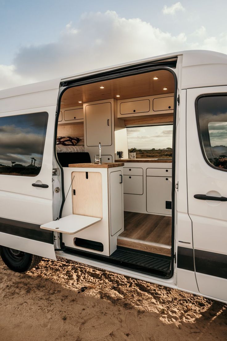 the interior of a white van with its doors open on a dirt ground near water