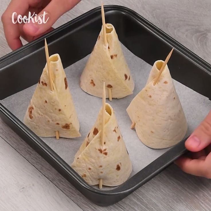 four burritos sitting on top of a pan with toothpicks stuck in them