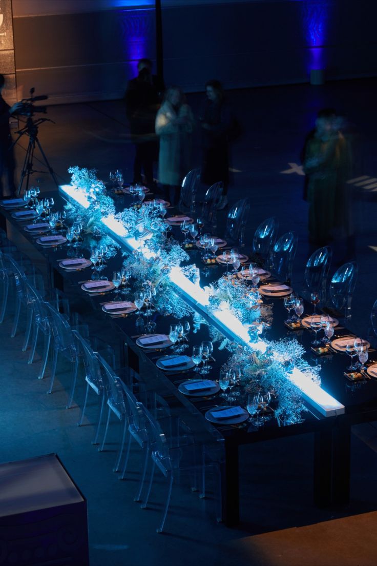 a long table is set up with clear chairs and blue lights in the dark room