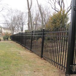 a black iron fence in the middle of a yard with grass and trees behind it