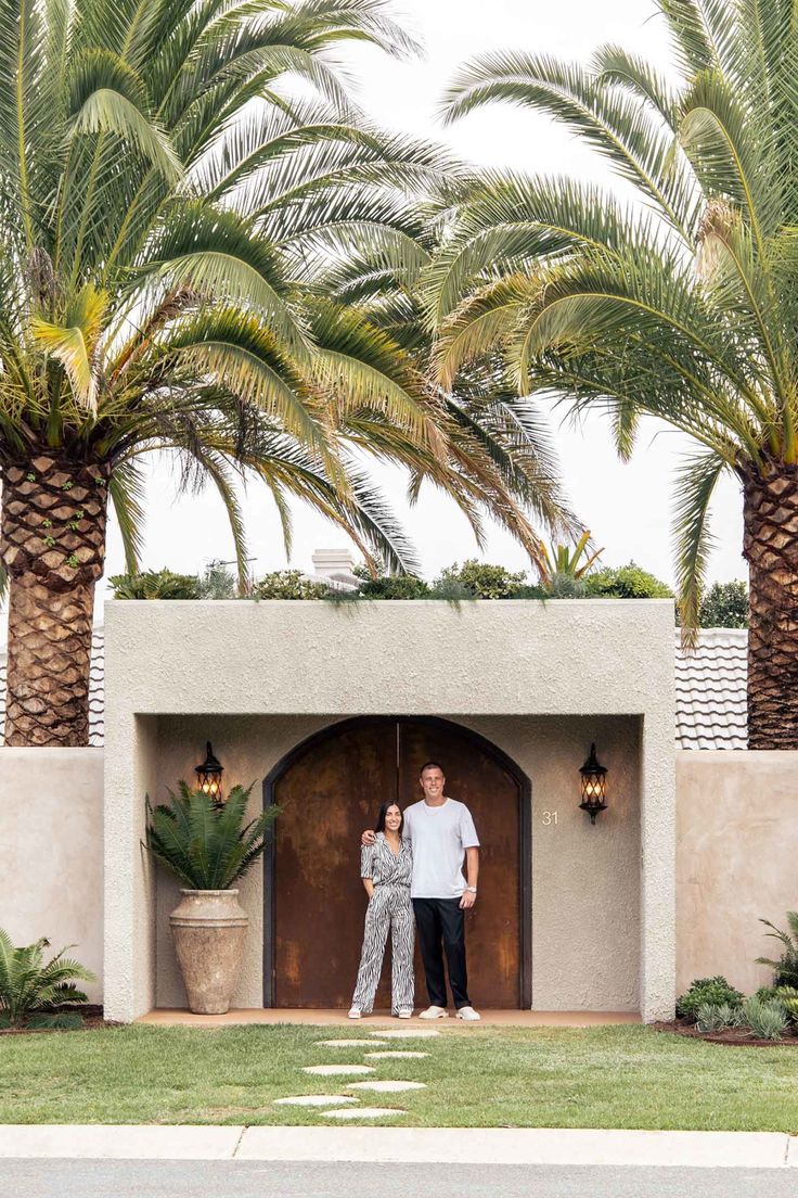 a man and woman standing in front of a building with palm trees behind them on a cloudy day