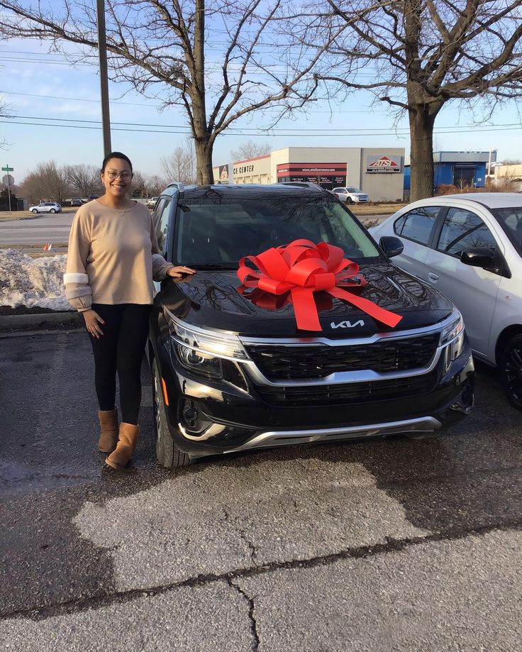 a woman standing next to a car with a red bow on it