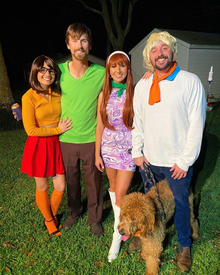 three people and a dog are posing for a photo in the yard at night time