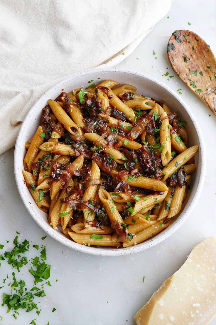 a white bowl filled with pasta and sauce on top of a table next to bread