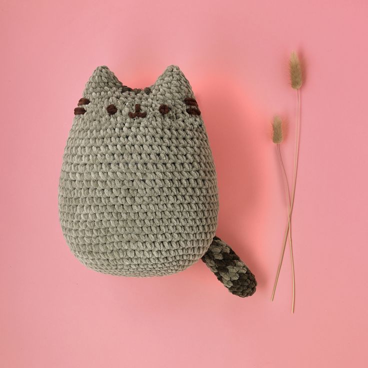 a crocheted cat pillow sitting on top of a pink surface next to a plant