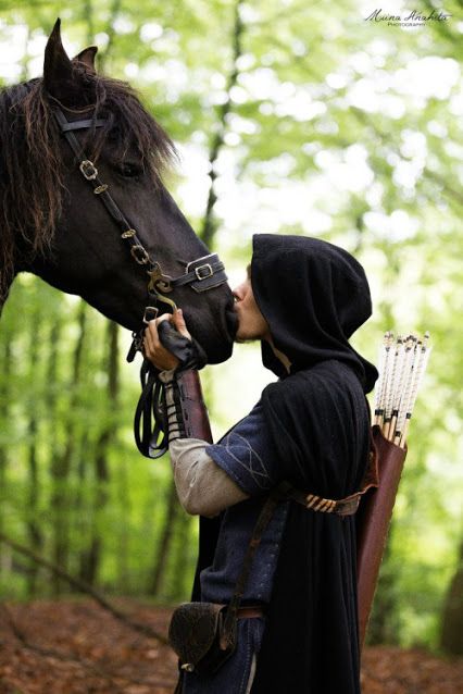 a woman in medieval garb kissing a horse's nose while standing next to a forest