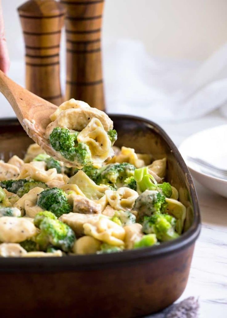 a wooden spoon full of pasta and broccoli in a casserole dish