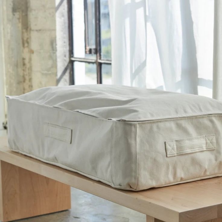 a mattress sitting on top of a wooden table in front of a window with curtains