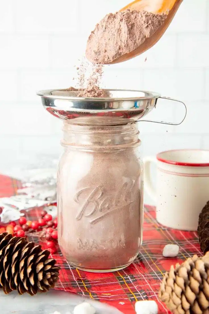 a spoon pouring sugar into a mason jar with pine cones and other holiday decorations around it