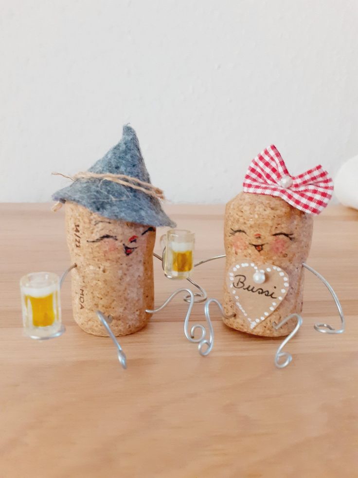 two wine corks with faces on them, one holding a glass and the other holding a mug