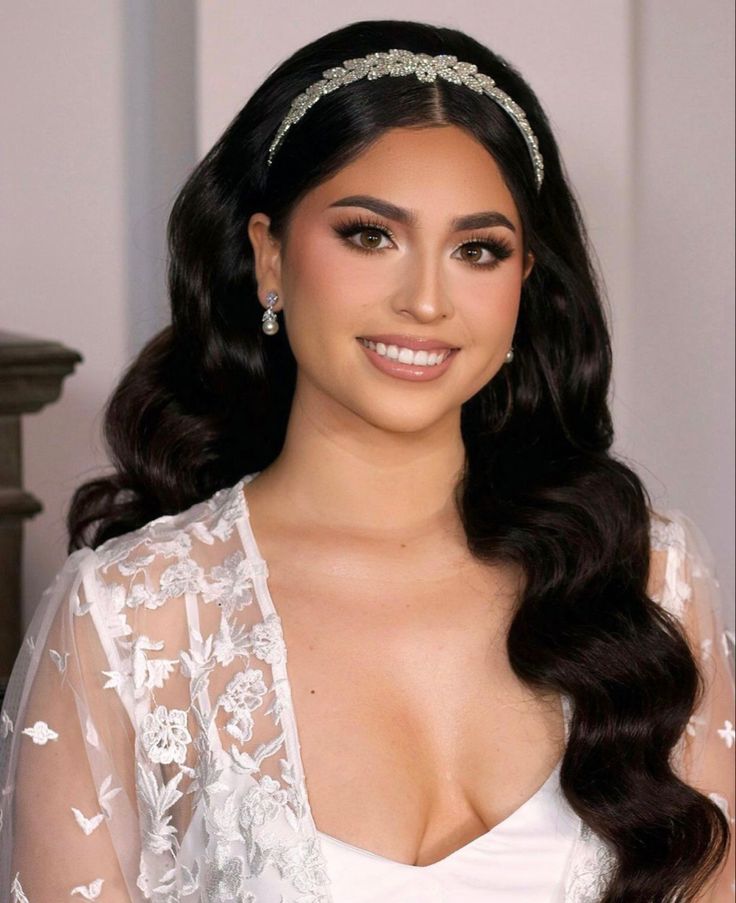 a woman with long dark hair wearing a white dress and headband, smiling at the camera